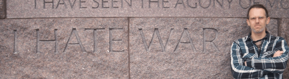Image of author standing next to FDR's Washington DC memorial wall which reads I Hate War